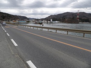 石巻女川線の現道。海側の道路より低い位置をＪＲの線路が並走している。ここから浦宿橋を架ける。海上では下部工の一部が施工中